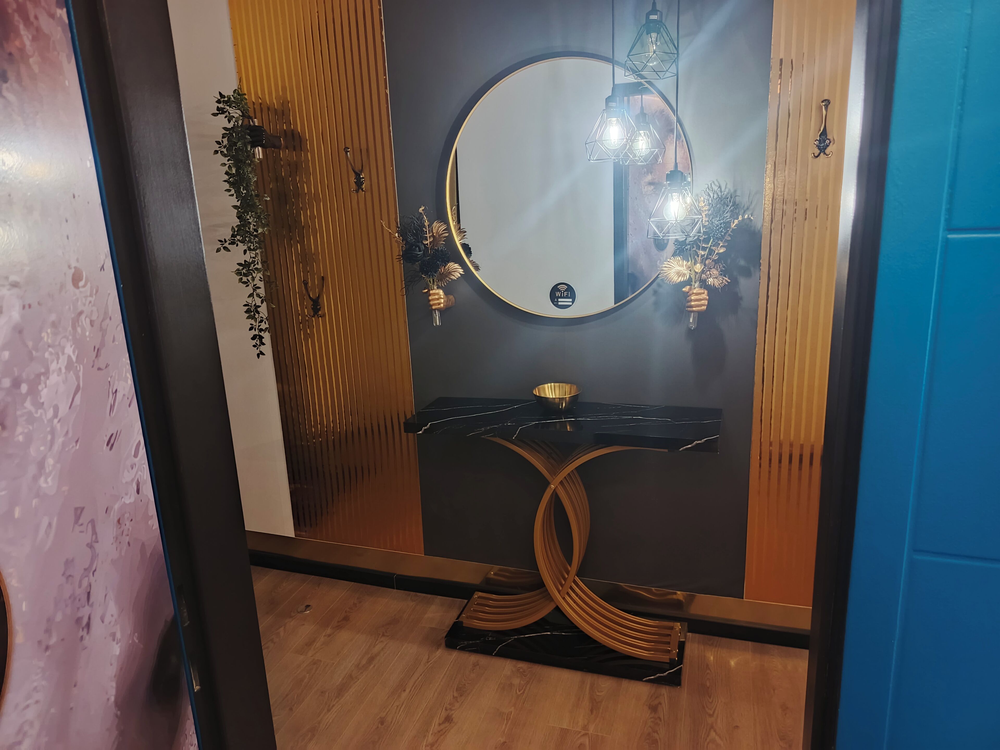 Une salle de bain avec un miroir rond, un lambris en bois, un lavabo en marbre noir et un récipient doré.