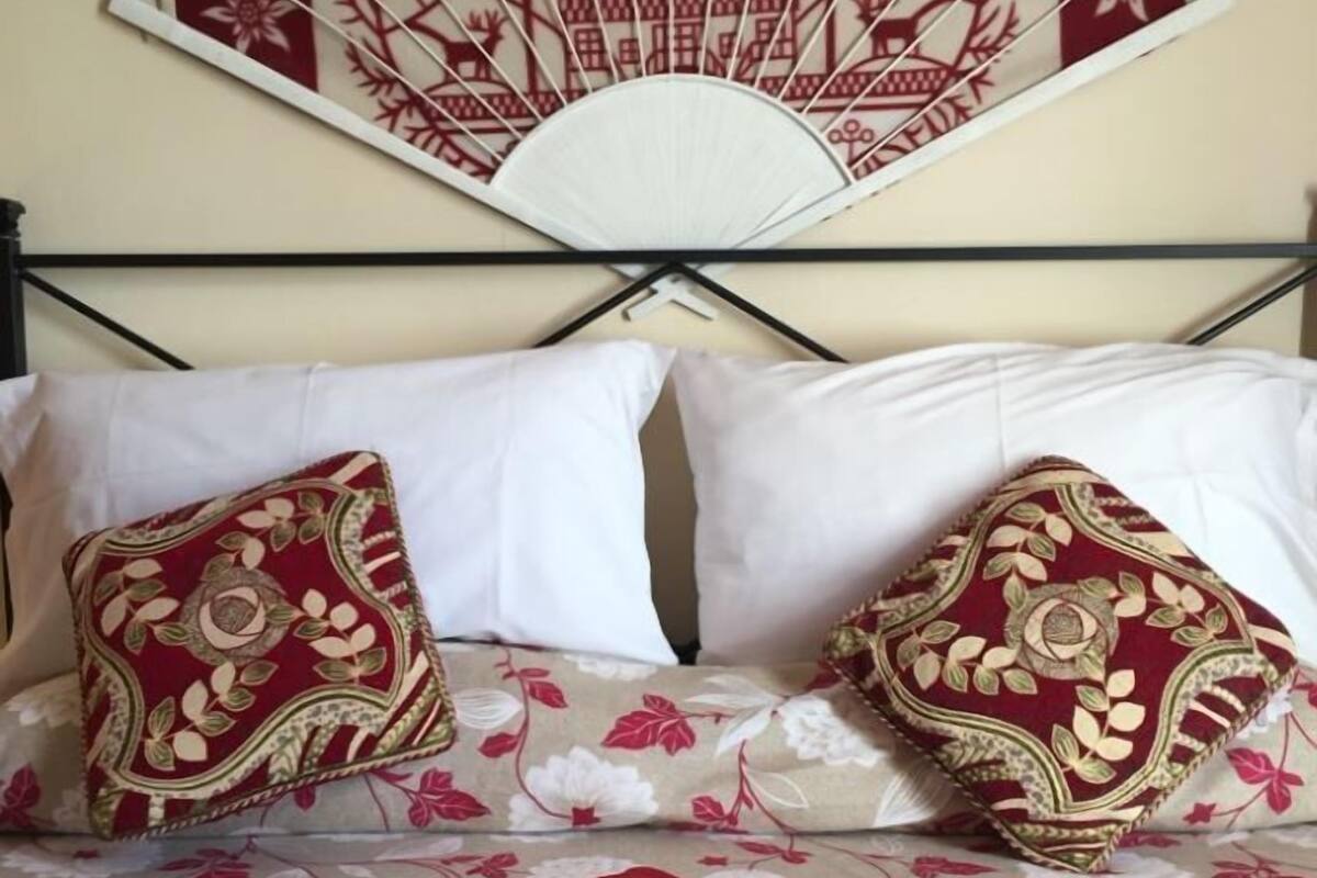 Una cama con ropa de cama floral, dos almohadones decorativos y un ventilador de pared con diseño de árbol.