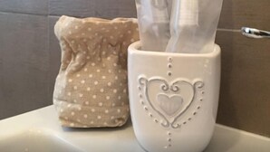 Een badkamer met een witte wastafel, een beige doek met stippen en een witte papieren zakjeshouder met een hartmotief.