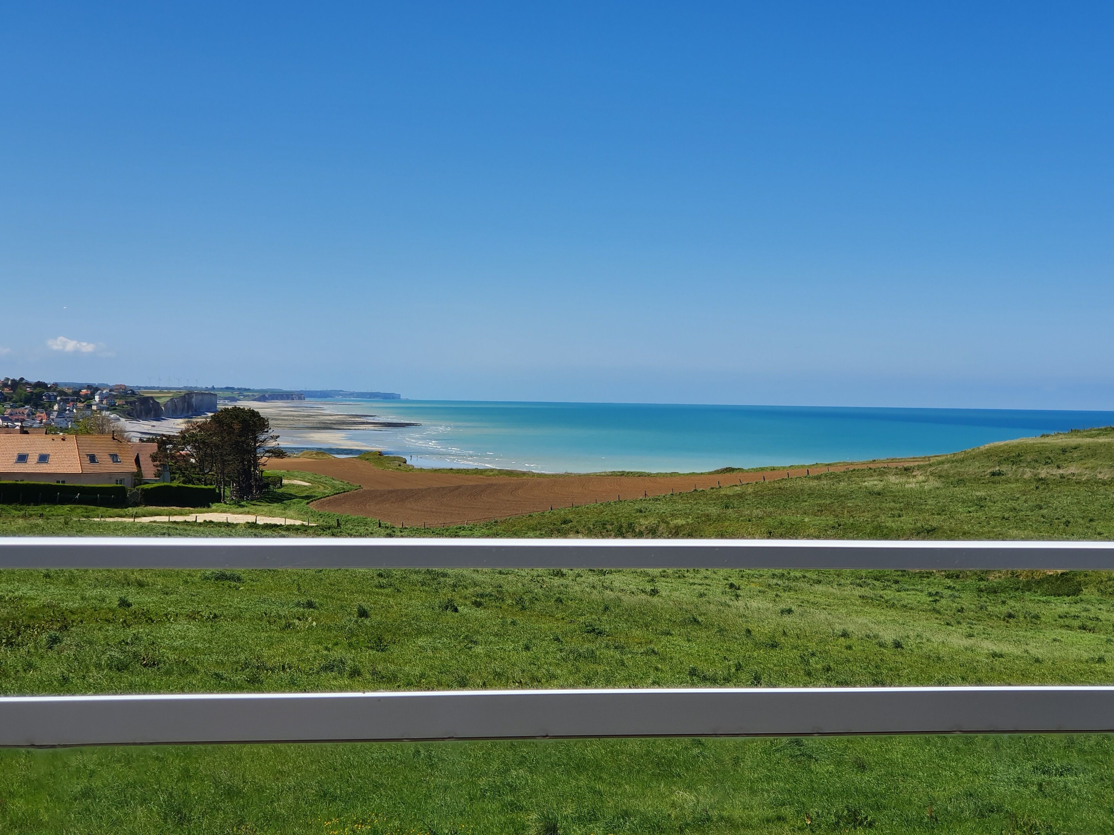 A coastal landscape with a road in the foreground, a beach, and a distant town.