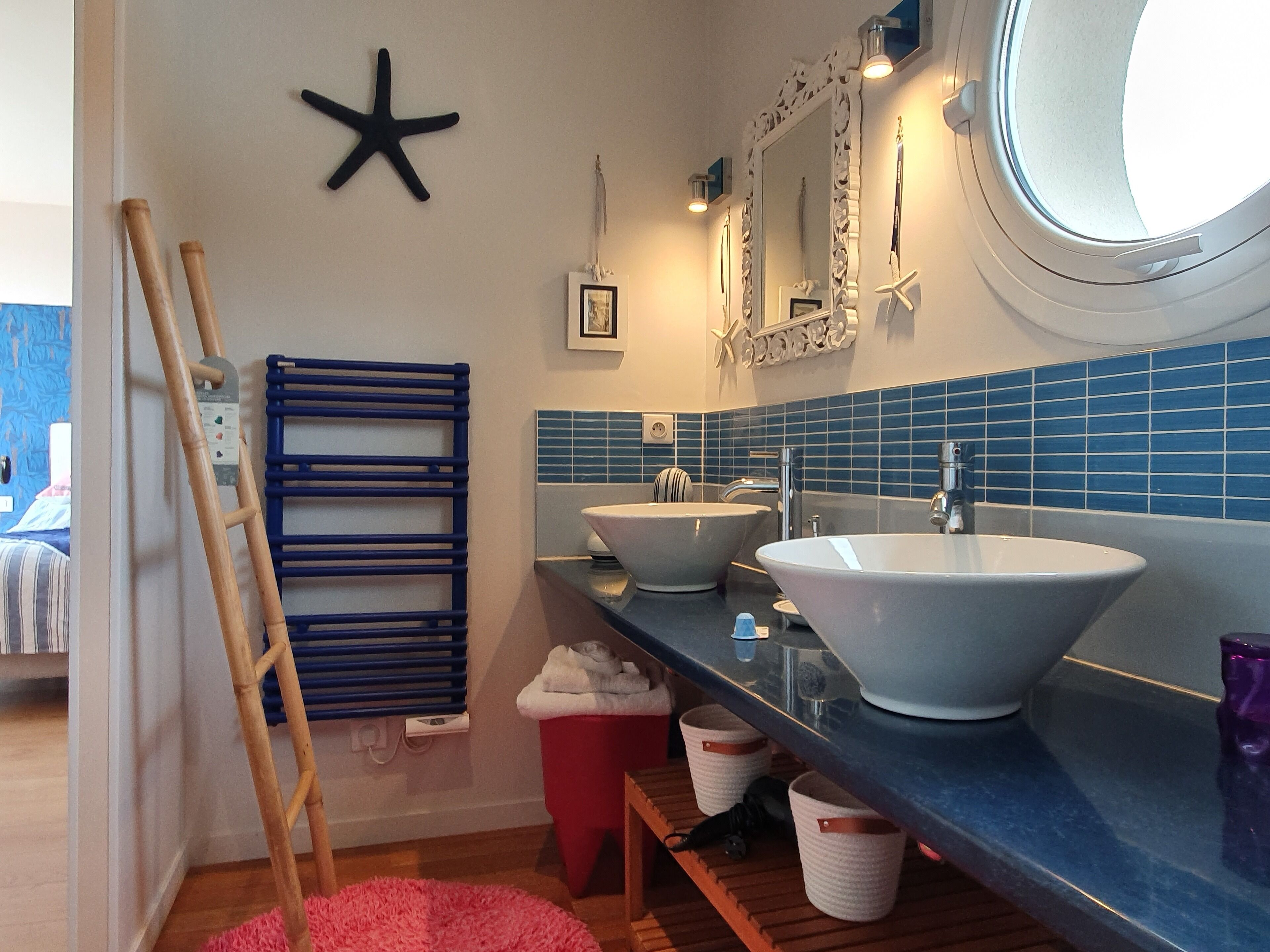 Une salle de bain avec un mur recouvert de carreaux bleus, deux lavabos, un grand miroir et une décoration en forme d’étoile de mer.