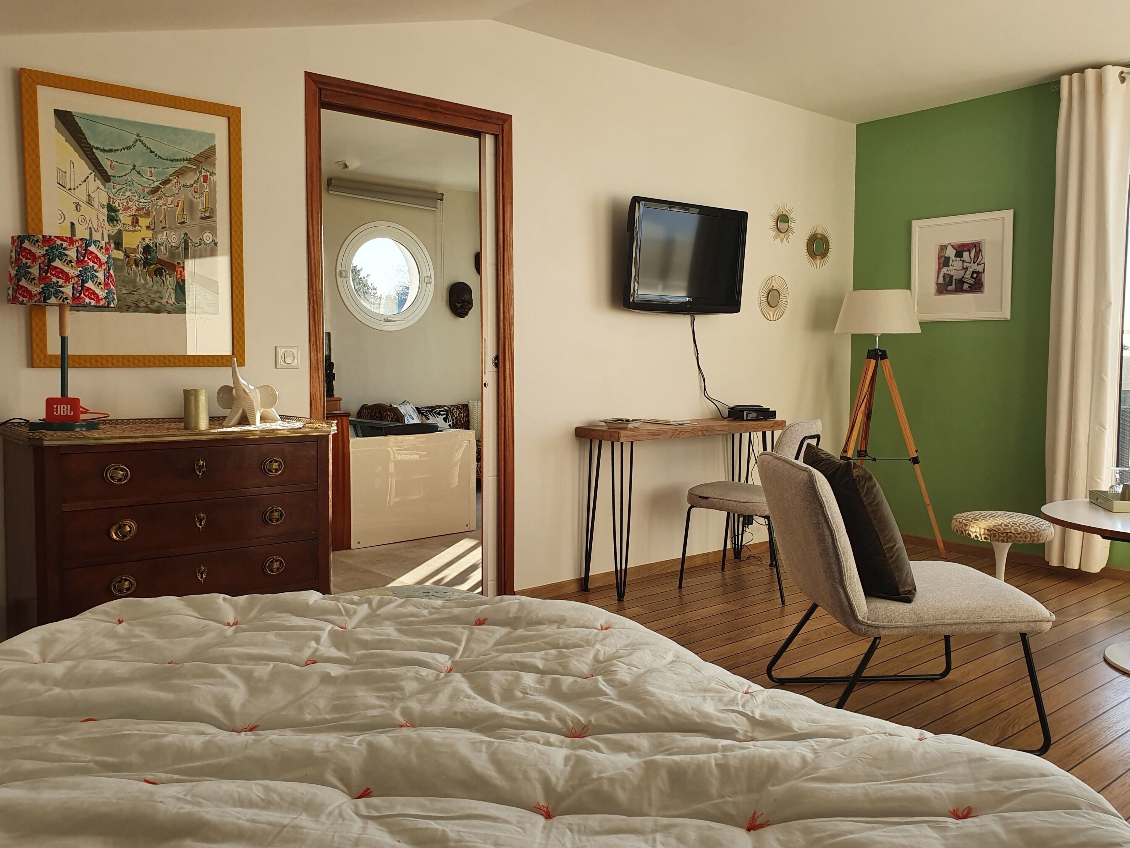 Un dormitorio con cama, cómoda, escritorio, silla y televisor en la pared.