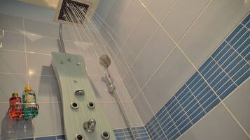 Un espace douche équipé d’un pommeau de douche à main, d’un panneau de commande fixé au mur et d’un mur recouvert de carreaux avec un motif bleu.
