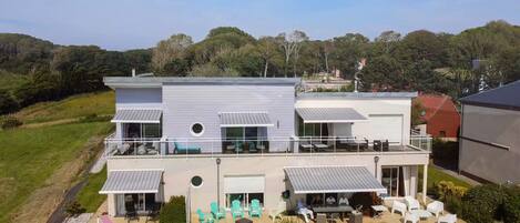 A modern two-story house with a balcony, outdoor seating, and a landscaped garden.