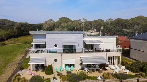 A modern two-story house with a balcony, outdoor seating, and a landscaped garden. - Fenêtres Sur Mer (Sainte-Marguerite-sur-Mer)