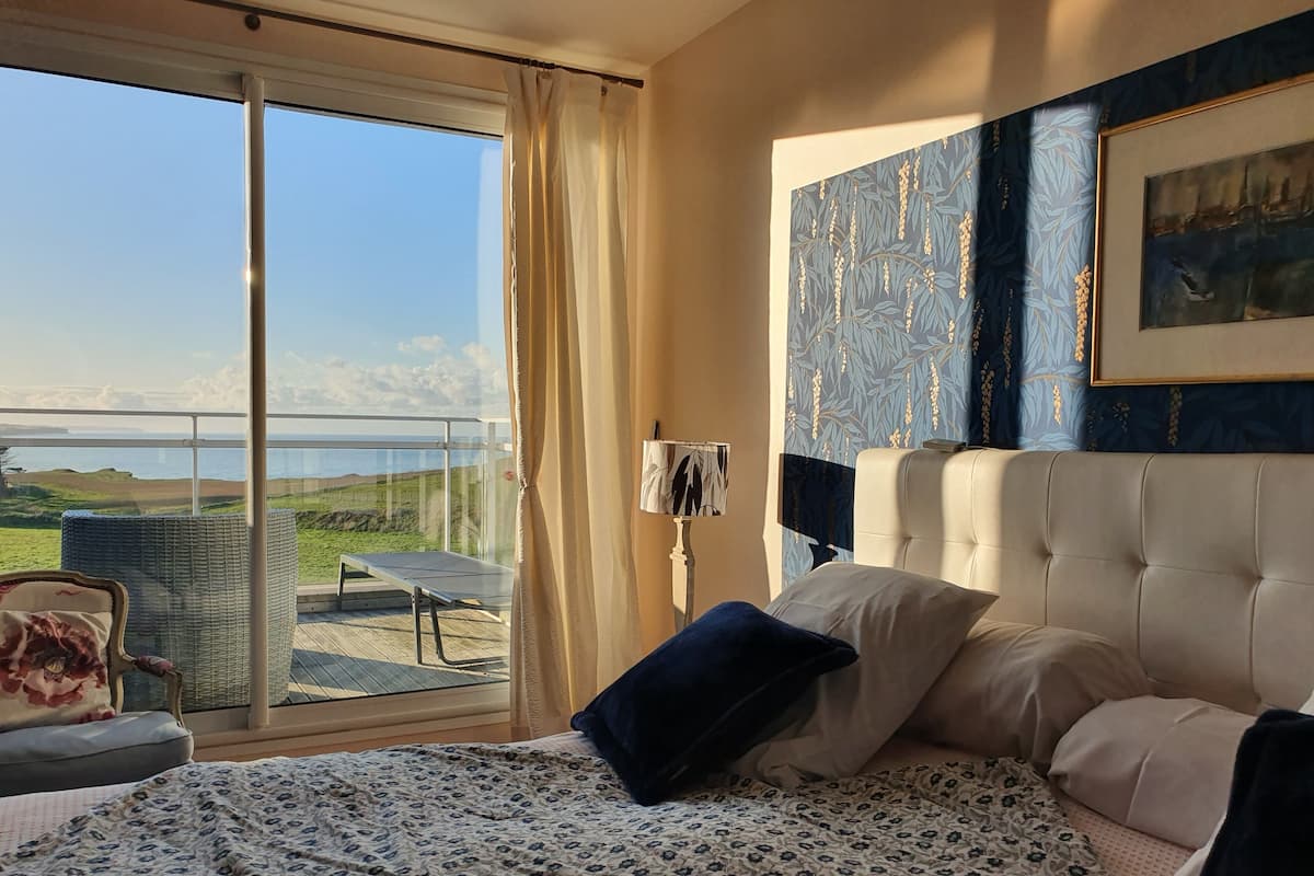 Un dormitorio con cama, una silla, una mesa y vista al mar.