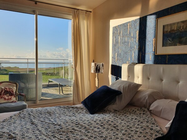 A bedroom with a bed, a chair, a table, and a view of the sea. - Fenêtres Sur Mer (Sainte-Marguerite-sur-Mer)