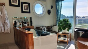 Un espacio habitable moderno con una isla de cocina, un sofá con cojines estampados, un amplio ventanal con cortinas y vistas al exterior.