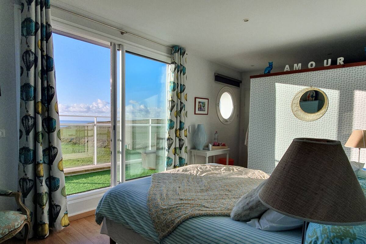 Un dormitorio con una cama grande, una mesita de noche, una lámpara, un espejo y vistas al exterior.