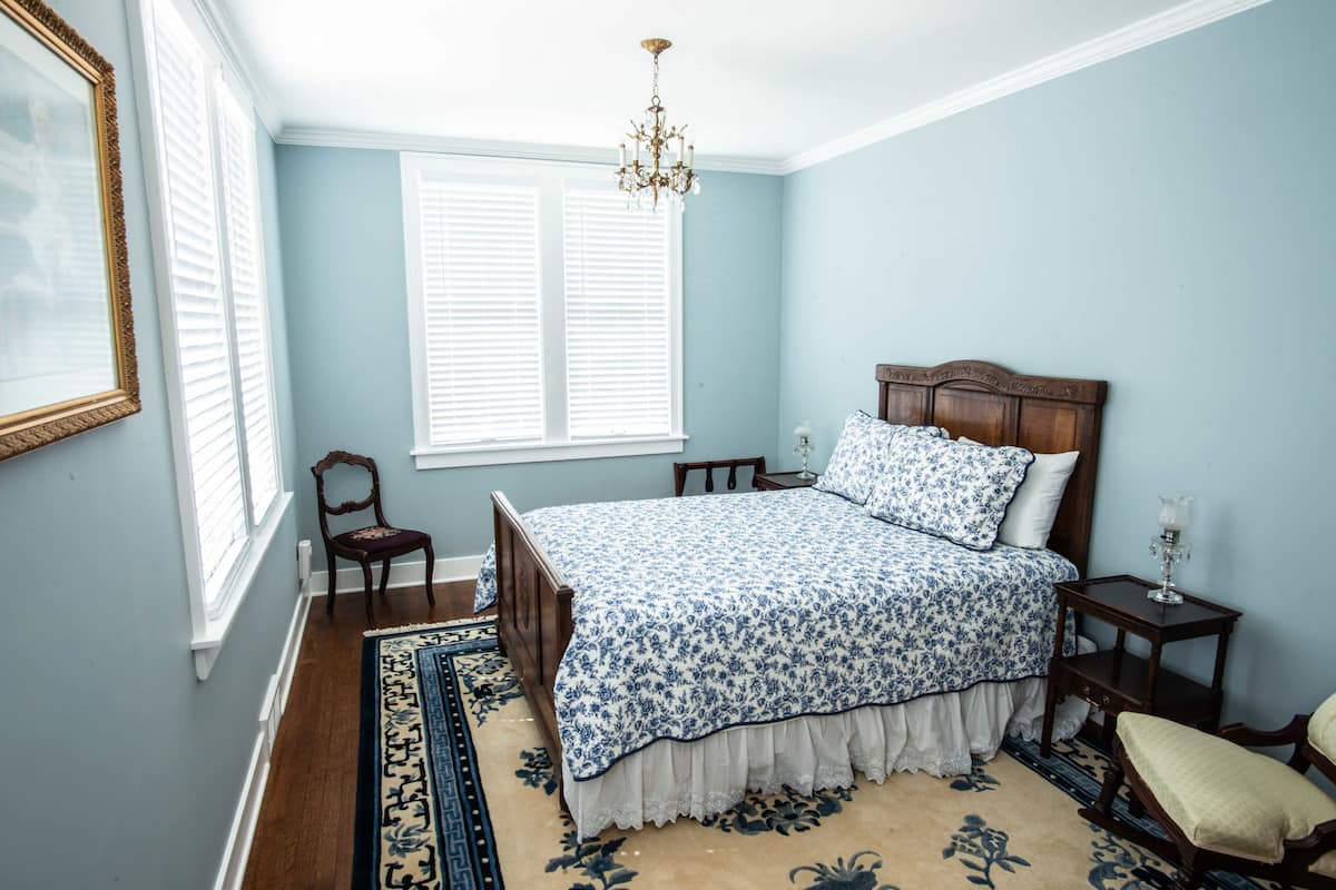 A bedroom with a large bed, a wooden chair, a nightstand, and a chandelier.