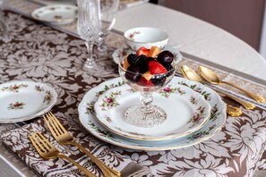 A table set with floral-patterned tablecloth, a glass bowl of fruit, and gold cutlery. - Valparaiso Inn Bed & Breakfast (Valparaiso)