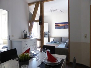 Un coin repas avec une table dressée pour deux personnes, un canapé en arrière-plan et un tableau au mur.