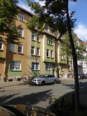 A multi-story building with a green and beige facade, multiple windows, and a parked white car on the street.