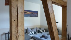 Quarto com estrutura de teto em madeira, sofá com almofadas listradas e um quadro na parede.