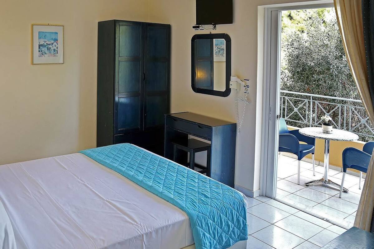 A hotel room with a bed, a desk, a chair, and a balcony with a table and chairs.