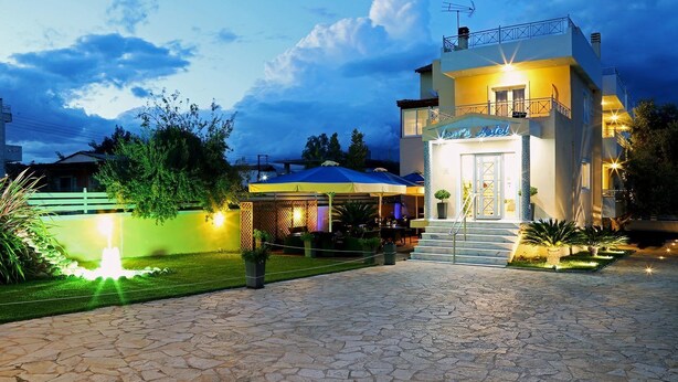 Un hotel con una entrada bien iluminada, un área de estar al aire libre techada y un camino empedrado de piedra que conduce a la entrada.