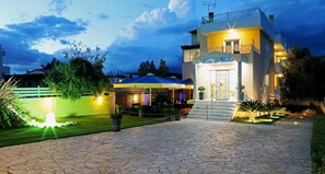 Un hotel con una entrada bien iluminada, un área de estar al aire libre techada y un camino empedrado de piedra que conduce a la entrada.