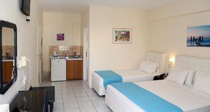 A hotel room with two beds, a small desk, a mirror, a TV, a kitchen area, and artwork on the walls.