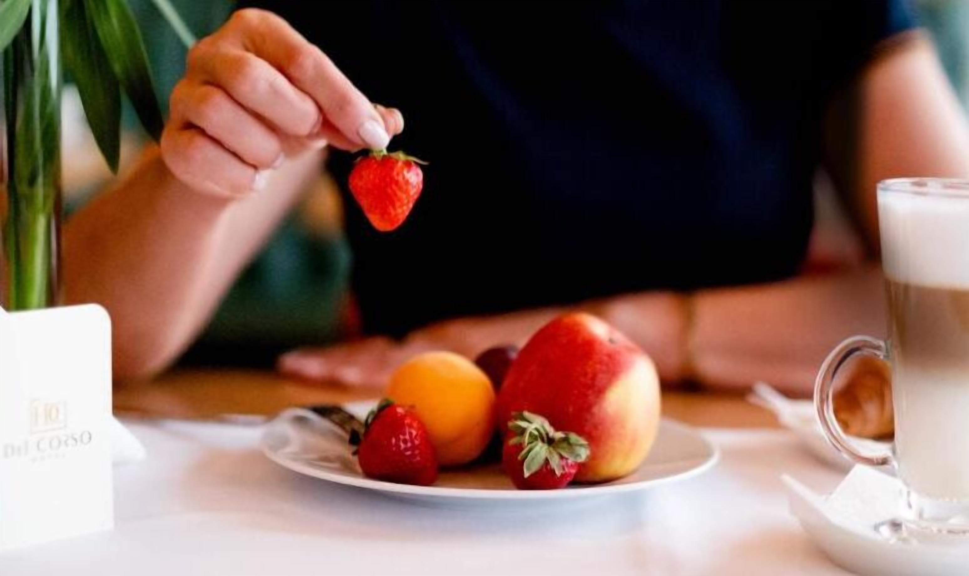 Un plato con fresas, melocotones y una naranja sobre una mesa.