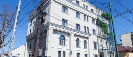 A multi-story building with a classic architectural style, featuring a central entrance with a glass facade, multiple windows, and a visible balcony on the upper floors.
