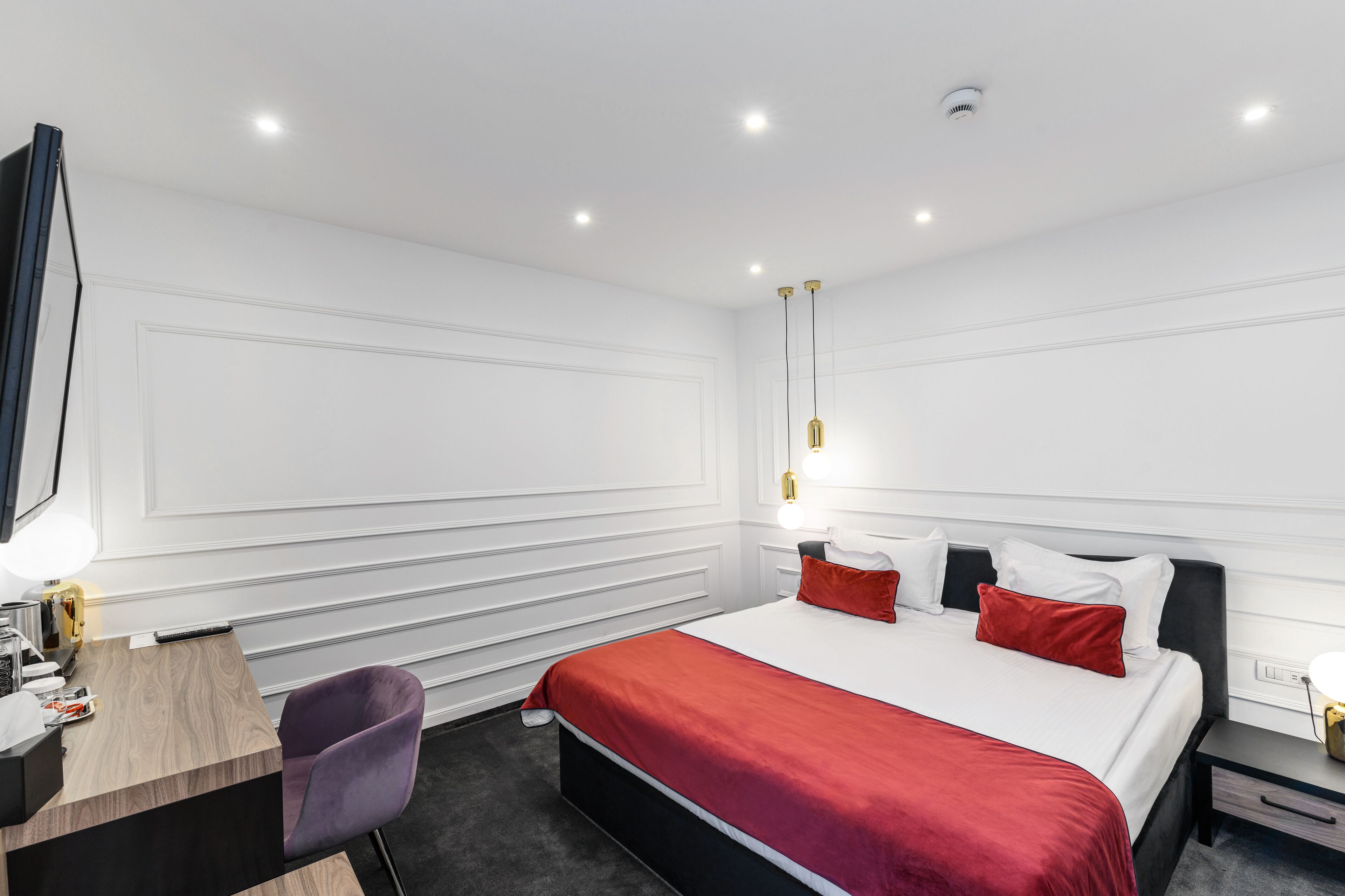 Una habitación de hotel con cama, mesita de noche, escritorio, silla y un espejo grande.