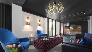 Una sala moderna con un otoman capitonado, un sillón azul y un sofá negro con cojines rojos y azules.
