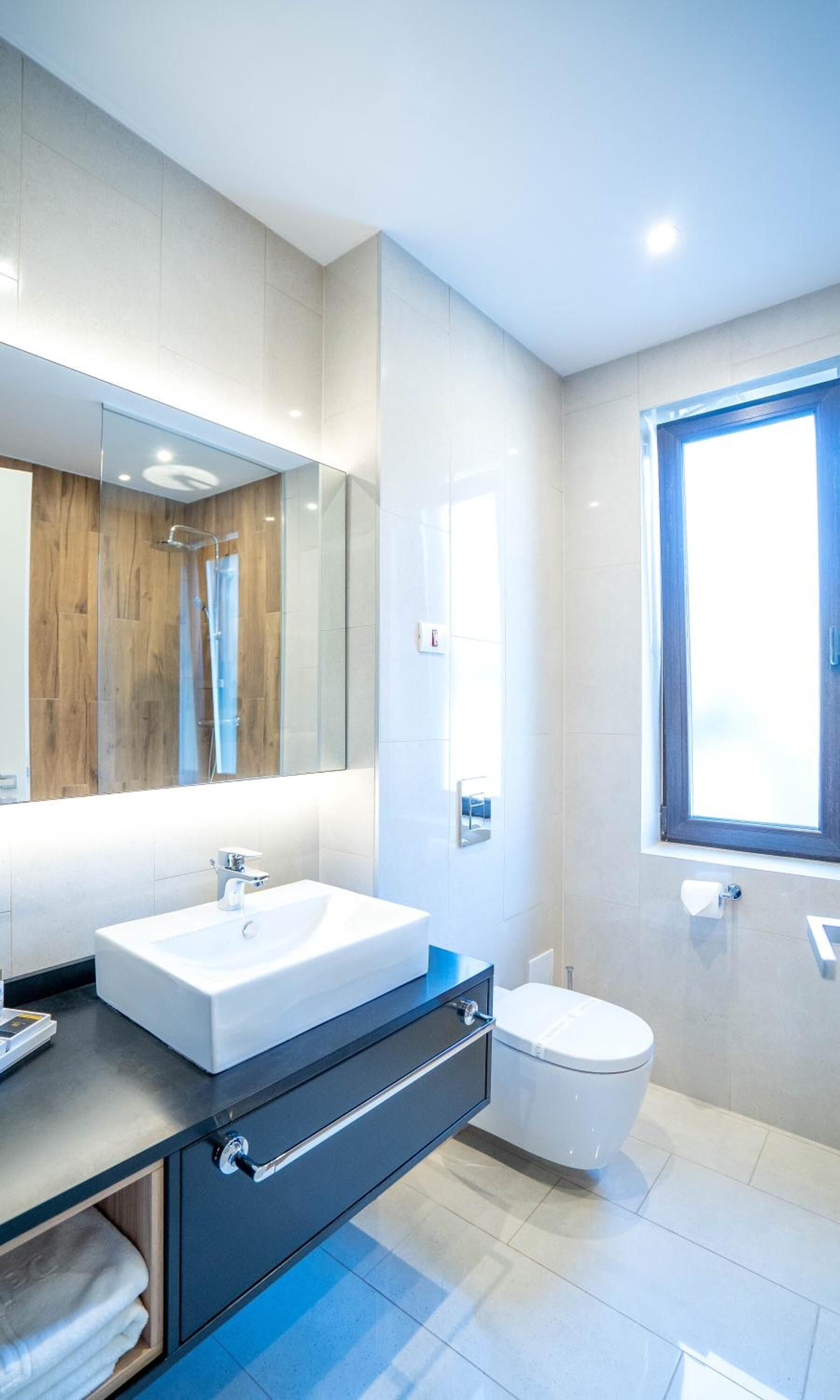 Une salle de bain moderne avec un grand miroir, un lavabo blanc, des toilettes et une fenêtre.