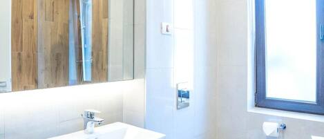 Une salle de bain moderne avec un grand miroir, un lavabo blanc, des toilettes et une fenêtre.