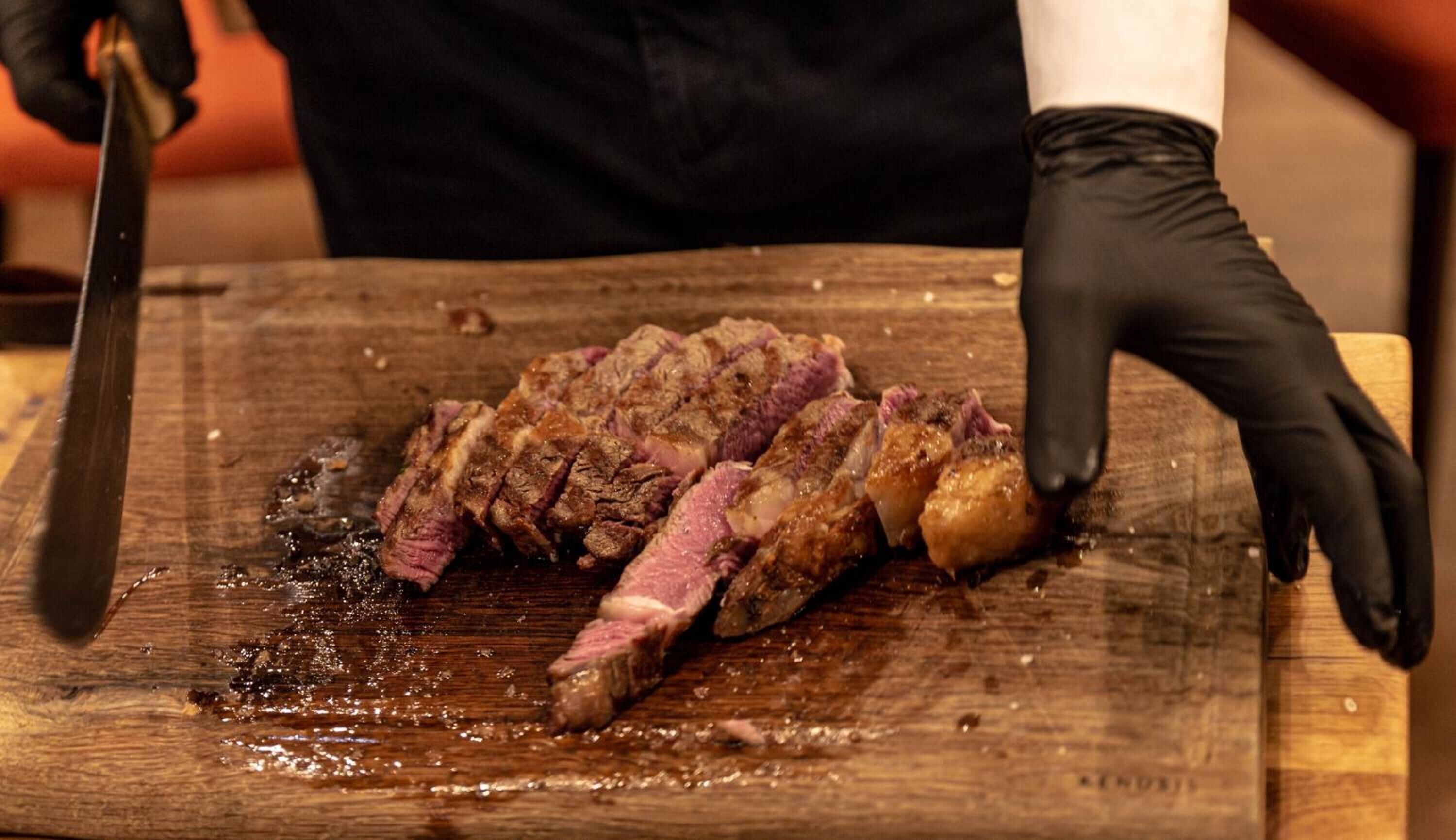 A person slicing a steak on a wooden cutting board.