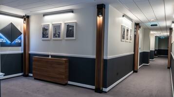 Un espace d’accueil moderne avec un comptoir en bois, des tableaux encadrés au mur et un panneau indiquant les coordonnées.