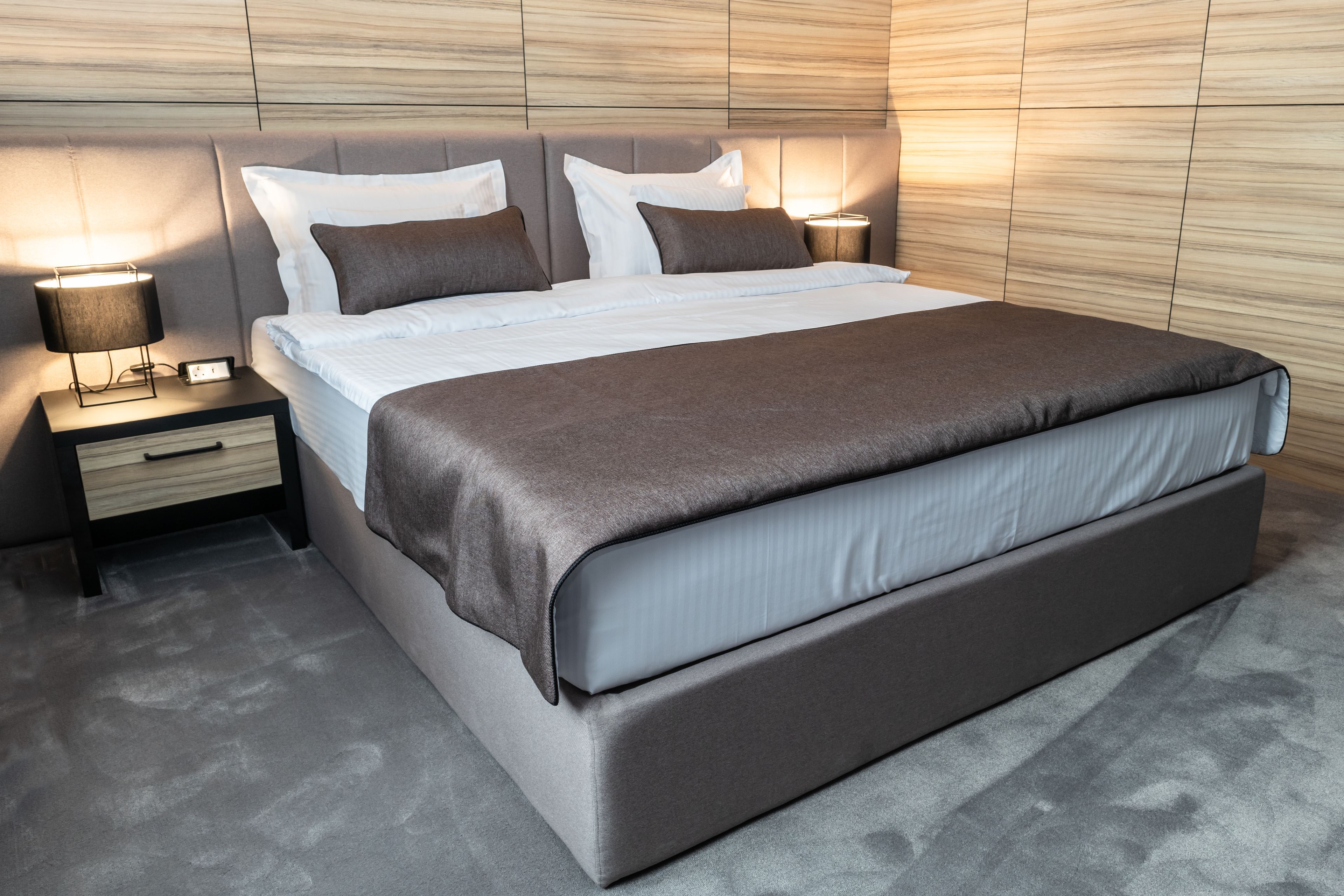 A modern bedroom with a large bed, nightstands, and a wooden headboard.