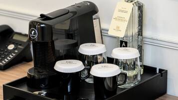 A coffee machine with four black coffee cups and a glass carafe on a tray.