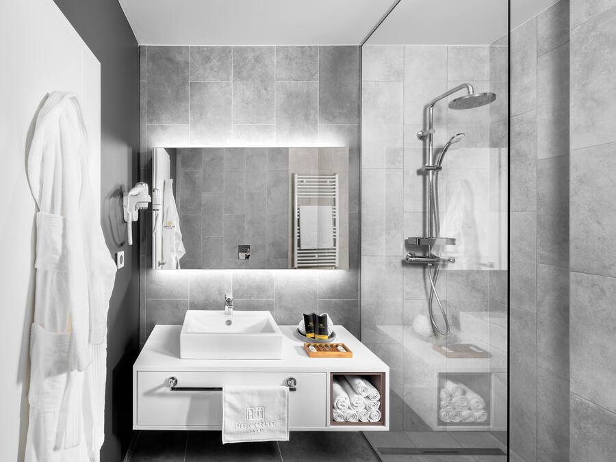 Un baño moderno con un espejo grande, un lavabo blanco, una ducha y un perchero para toallas.