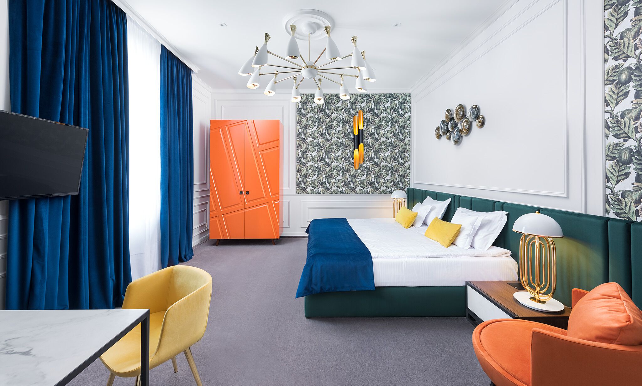 A hotel room with a bed, a desk, a chair, a TV, and a wall with a patterned wallpaper.