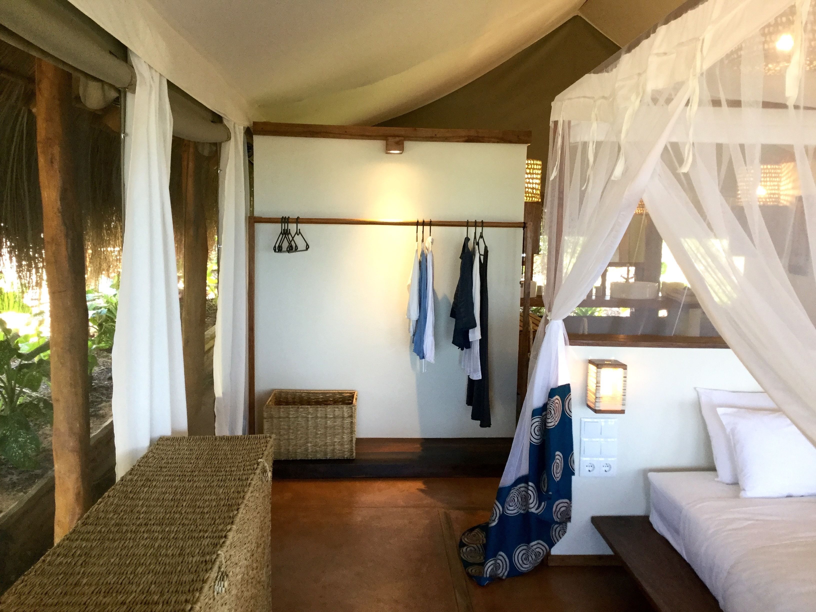 A bedroom with a bed, a hanging chair, a small table, a wardrobe, and a window with curtains.