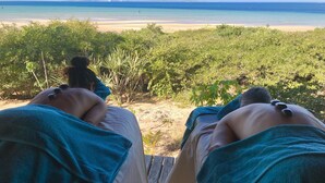 A person receiving a back massage with stones on their back, overlooking a beach with clear blue water and greenery. - asDunas Lodge (Vilanculos)
