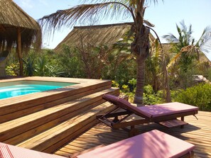 A wooden deck with a hot tub, lounge chairs, and thatched-roof structures.