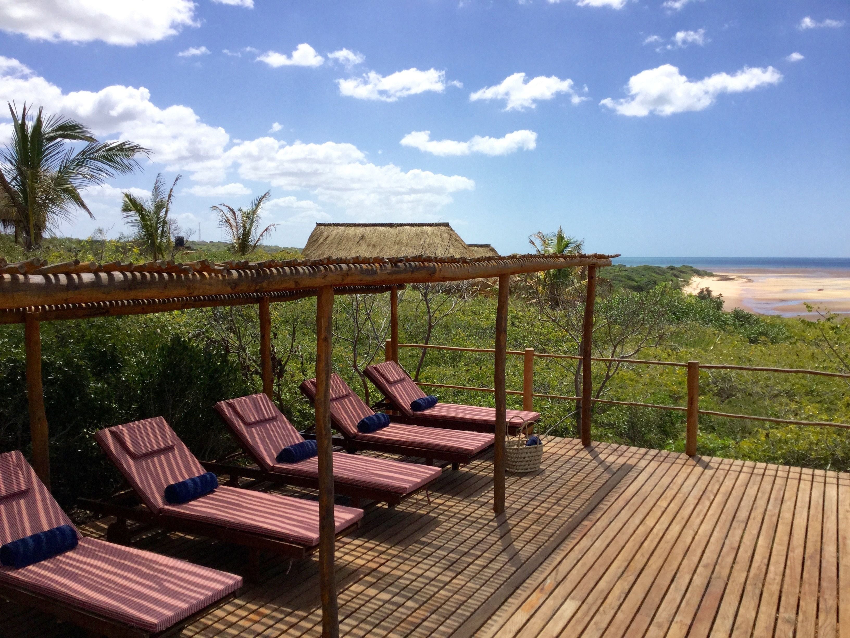 A wooden deck with striped lounge chairs and a thatched-roof structure.