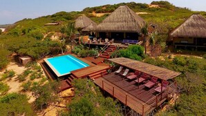 A resort with a pool, thatched-roof structures, and a wooden deck with lounge chairs. - asDunas Lodge (Vilanculos)