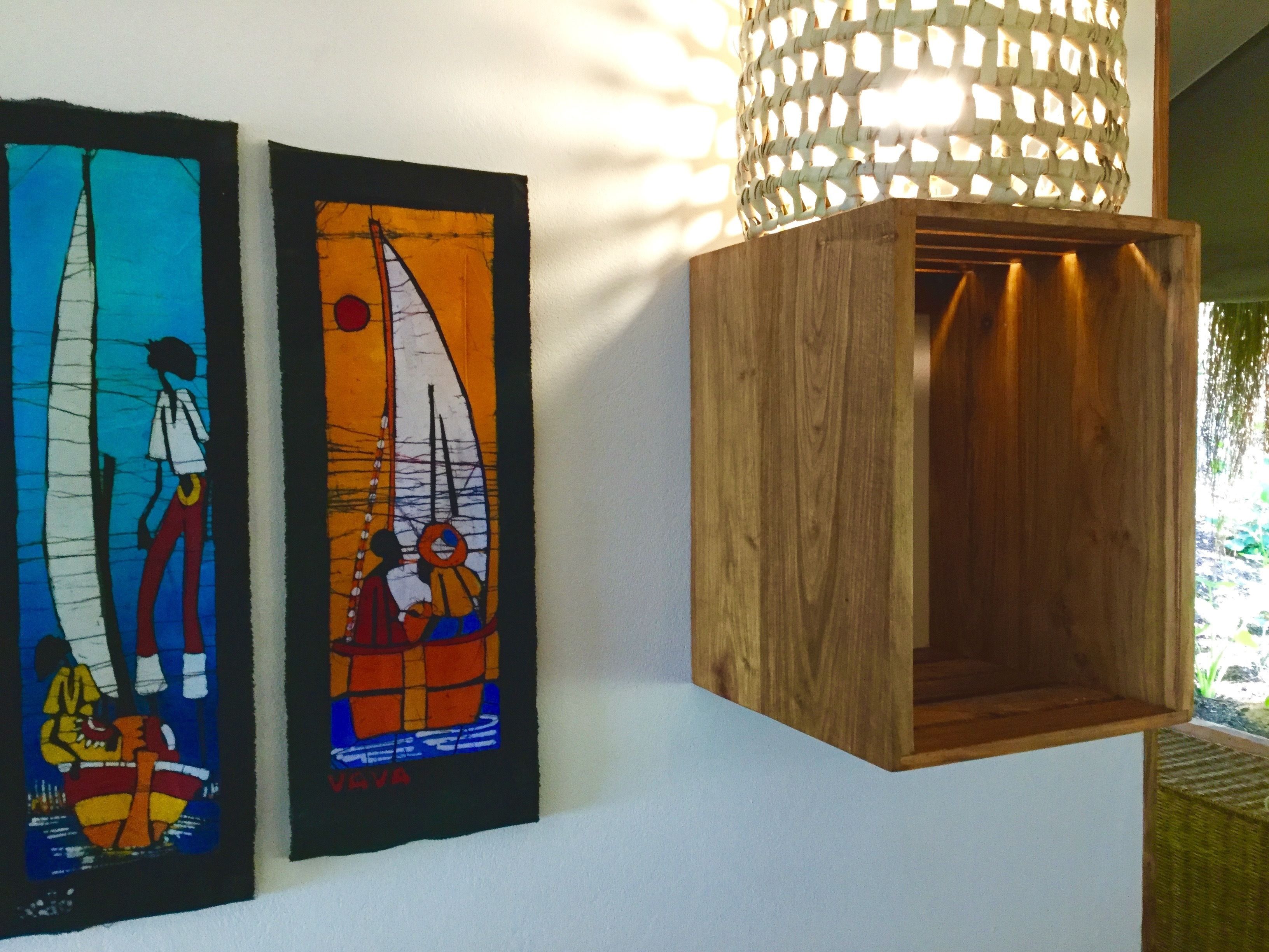Two framed artworks with sailboats and people, a wooden box, and a woven light fixture.
