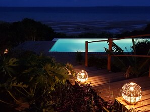 A pool with a wooden deck and a view of the ocean.