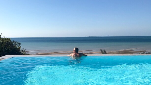A wooden deck leading to a clear blue infinity pool with a view of the beach and ocean. - asDunas Lodge (Vilanculos)