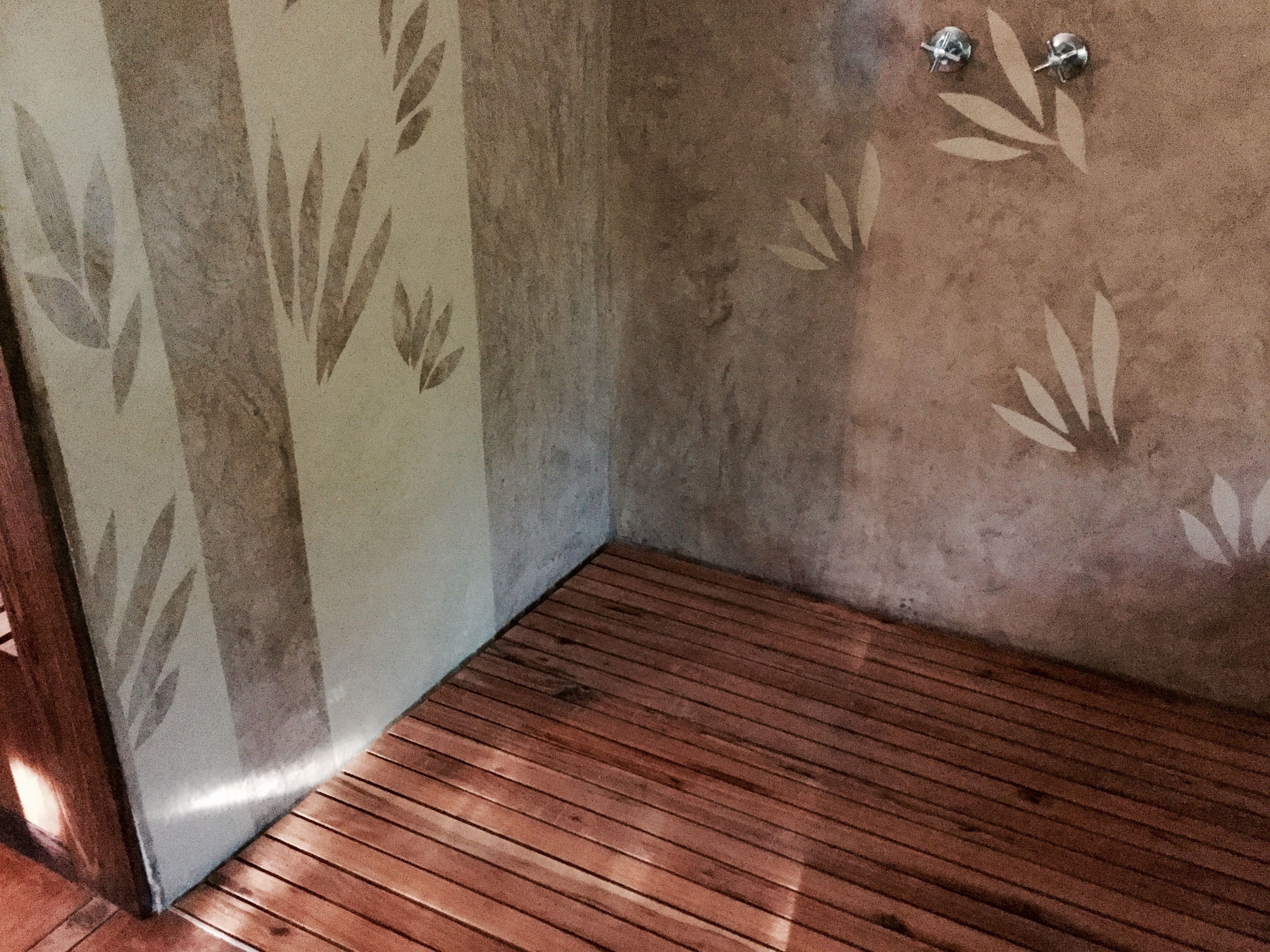 Un baño con suelo de madera, una pared con diseño de hojas y una esquina con perchero.