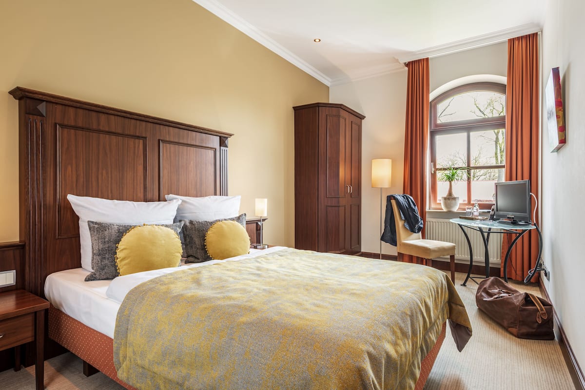 Ein Hotelzimmer mit einem großen Bett, einem Schreibtisch mit Computer, einem Stuhl und einem Kleiderschrank.