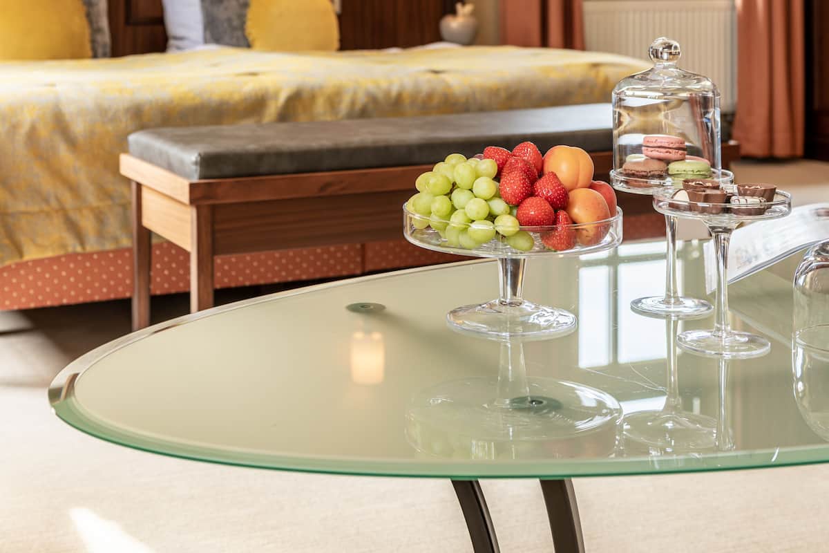 Ein Hotelzimmer mit Bett, Nachttisch und einem Glastisch mit Früchten und Desserts.