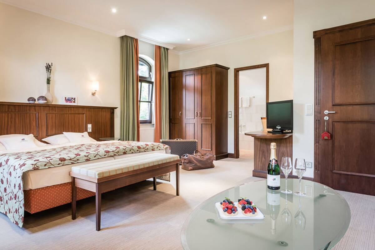 Ein Hotelzimmer mit Bett, einer Bank, einem Glastisch mit Flasche und Gläsern, einem Fernseher und einem Kleiderschrank.