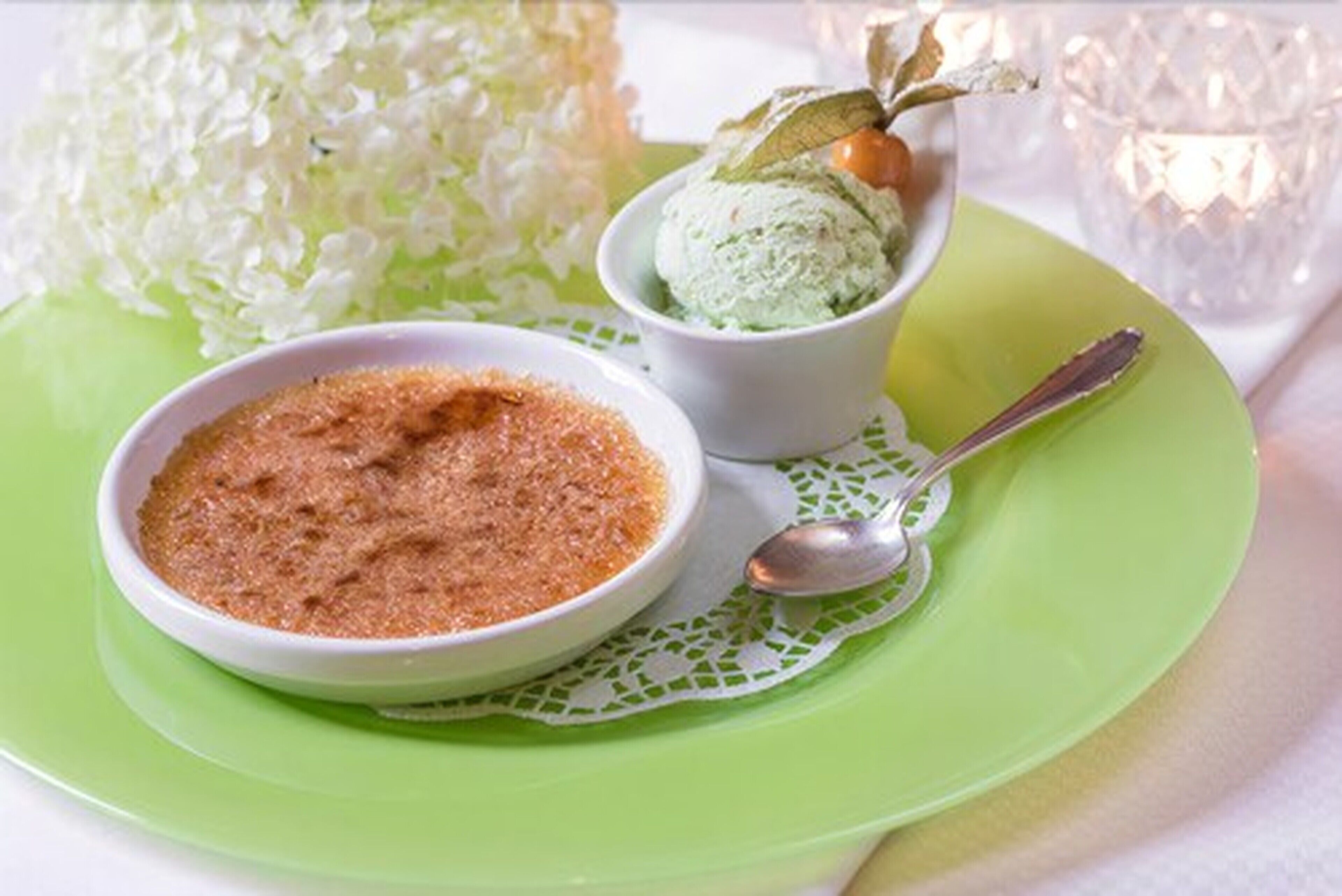 A dessert setup with a bowl of brown sugar and a bowl of green ice cream, accompanied by a decorative candle and a glass of water.