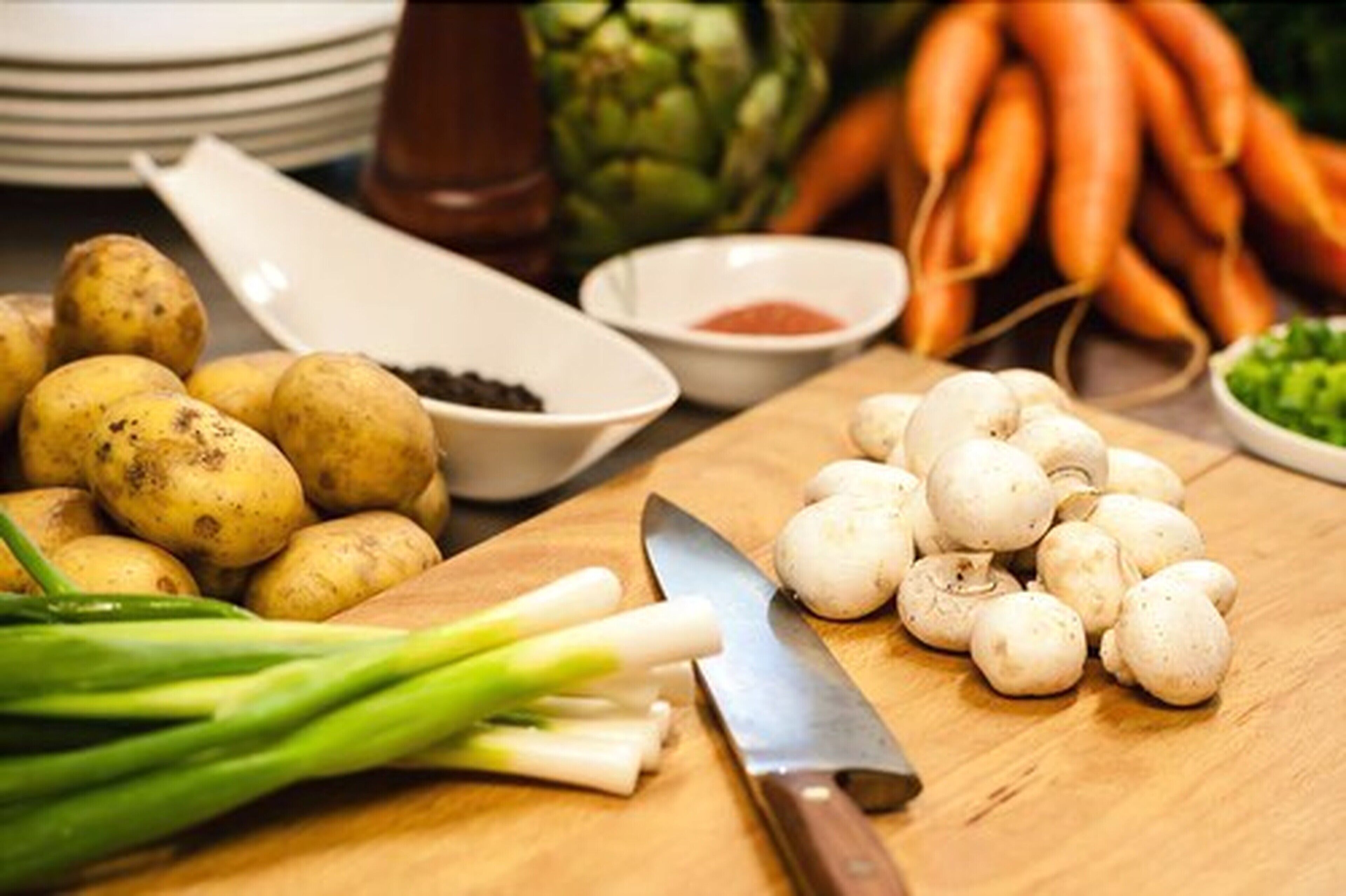 Uma tábua de corte de madeira com batatas, cogumelos e cebolinha.