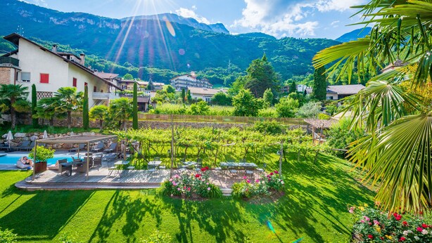 A lush garden with a pool, outdoor seating, and a view of mountains. - Gartenheim B&B Tramin (Termeno Sulla Strada del Vino)