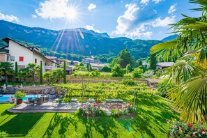 A lush garden with a pool, outdoor seating, and a view of mountains. - Gartenheim B&B Tramin (Termeno Sulla Strada del Vino)